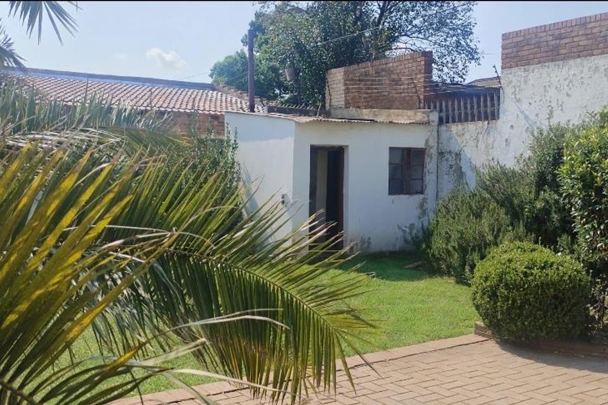 Rear garden area featuring a paved patio, lawn, and a small outbuilding against a brick boundary wall.