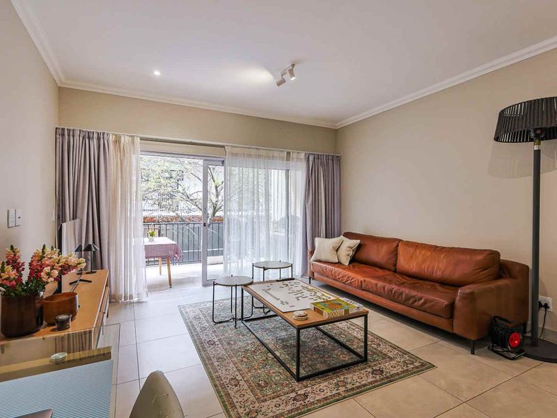 A well-maintained living room featuring tiled flooring, cove molding, and a large sliding glass door providing access to a balcony.