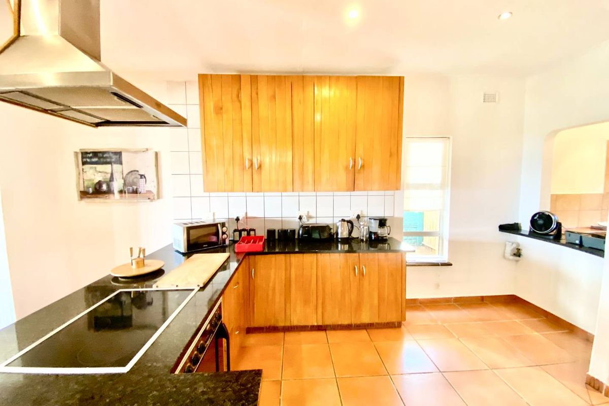 A functional kitchen featuring wooden cabinetry, granite countertops, a built-in hob, and a stainless steel extractor fan with tiled flooring.