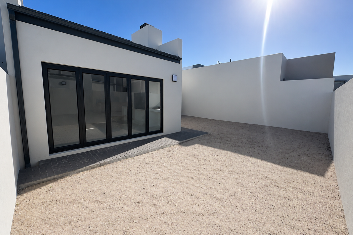 A modern rear exterior view featuring a paved patio area, large black-framed folding glass doors, and a low-maintenance gravel garden space.
