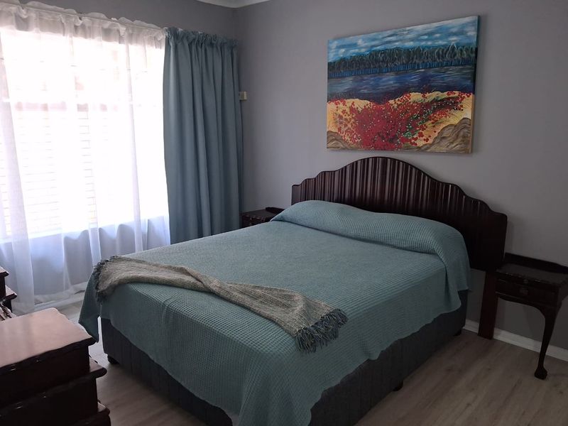 A well-maintained bedroom featuring light-toned laminate flooring and a large window, providing a comfortable and neutral living space.