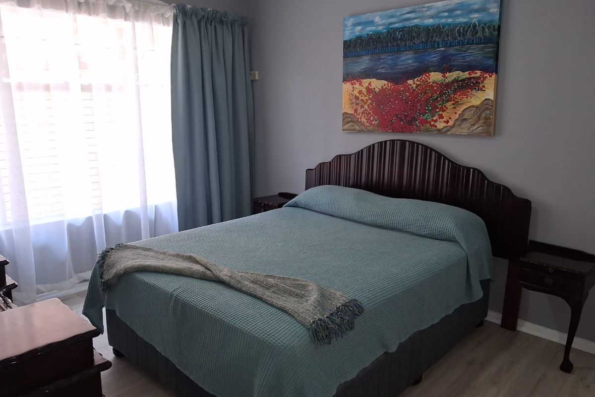 A well-maintained bedroom featuring light-toned laminate flooring and a large window, providing a comfortable and neutral living space.