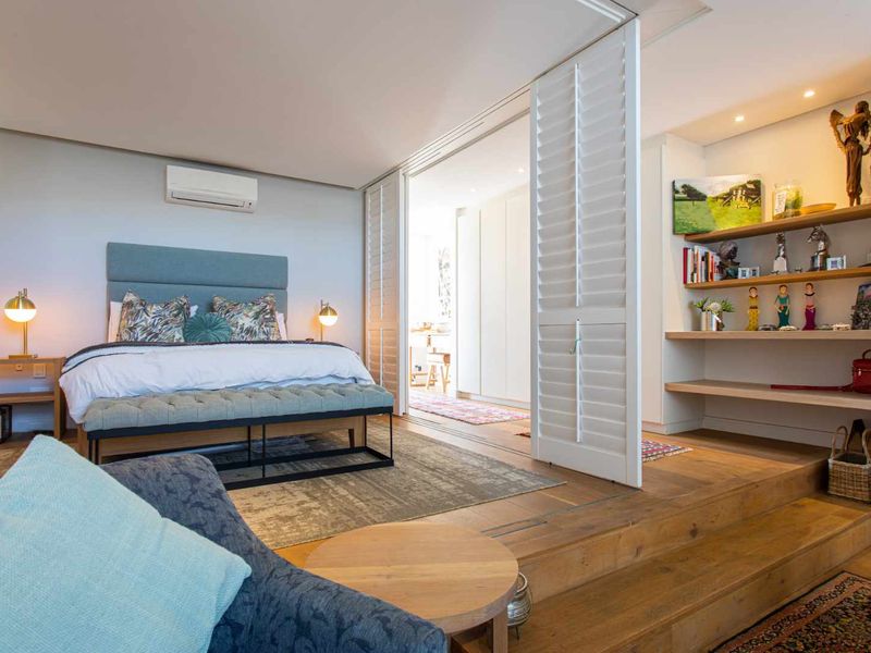 A well-appointed bedroom featuring timber flooring, a raised platform area with built-in shelving, and plantation shutters separating the space.