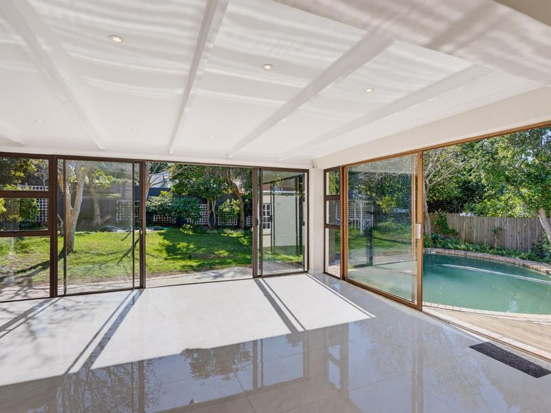 Bright and spacious living area featuring large sliding glass doors that open directly onto the garden and pool area, with modern tiled flooring.