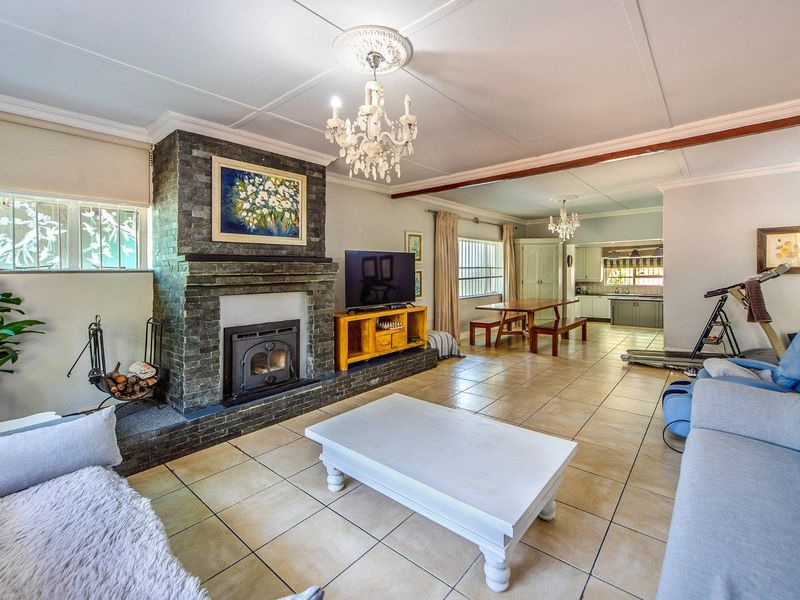 Spacious open-plan living area featuring a prominent stone-clad fireplace with a wood-burning stove, tiled flooring, and an integrated kitchen space in the background.