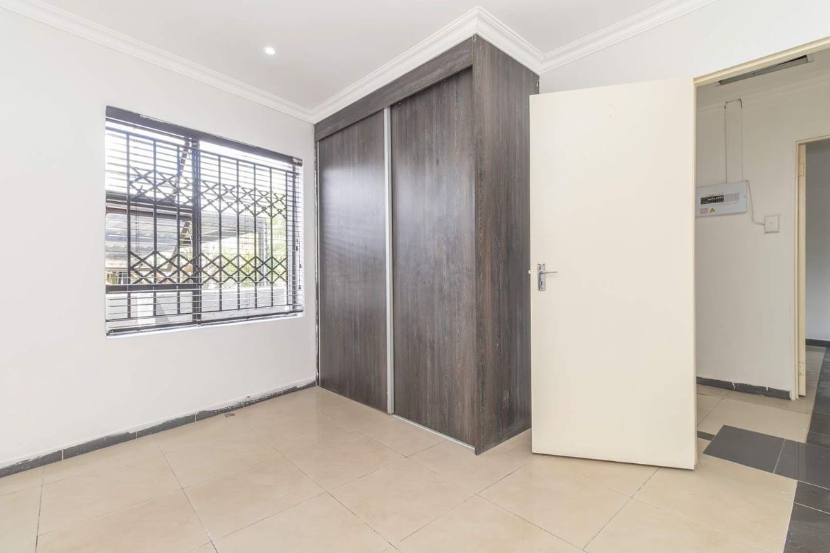 A bright, empty bedroom featuring tiled flooring, a built-in sliding door wardrobe, and a window fitted with a security gate.