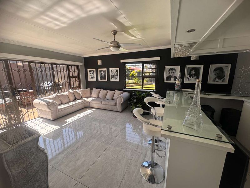 Open-plan living area featuring a built-in bar with glass counter, tiled flooring, ceiling fan, and direct access to the patio through security gates.
