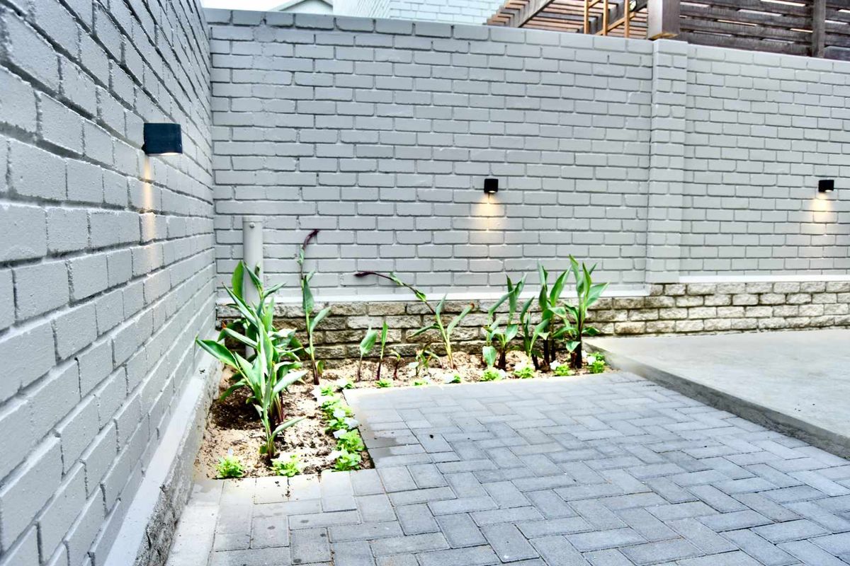 A private courtyard featuring paved flooring, a painted brick boundary wall, integrated wall-mounted lighting, and a small landscaped garden bed.