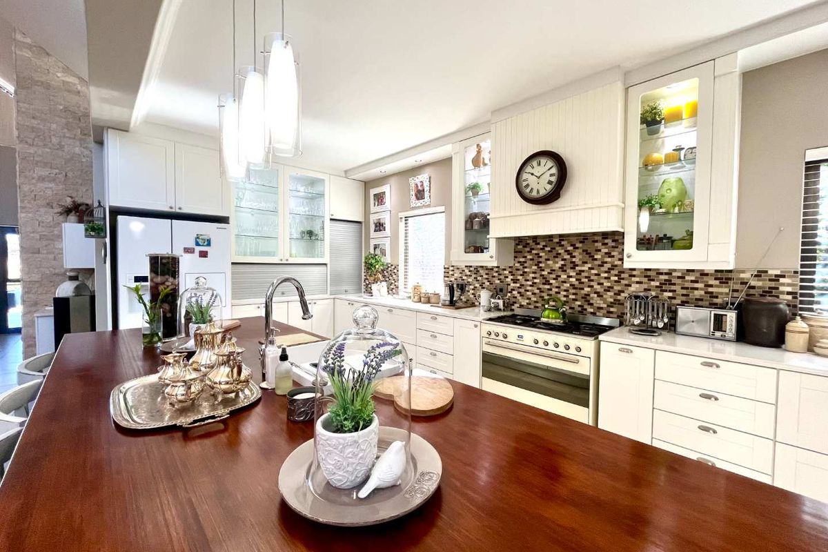 A well-appointed kitchen featuring a large wooden island, mosaic tile backsplash, built-in oven with extractor fan, and glass-fronted cabinetry with integrated lighting.