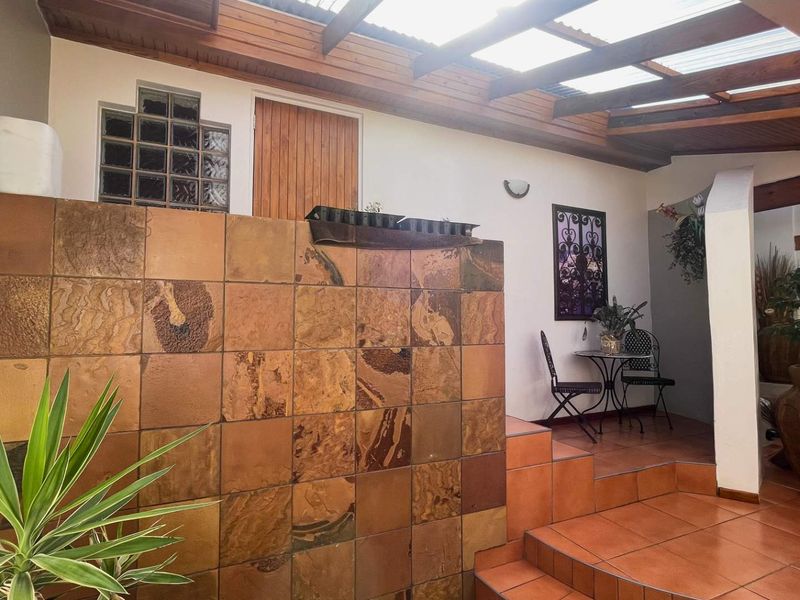 A covered patio area featuring a timber pergola, slate tile feature wall, and ceramic flooring, providing a sheltered outdoor space.