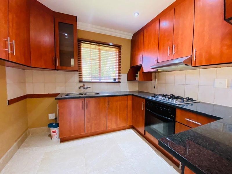 A functional kitchen featuring warm-toned wooden cabinetry, granite countertops, a gas hob, built-in oven, and a tiled backsplash with ample storage space.