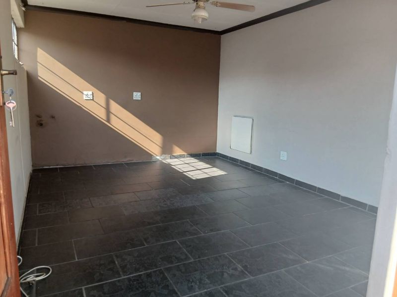 An empty living room featuring dark tiled flooring, a ceiling fan, and a wall-mounted heater, offering a blank canvas for interior design.