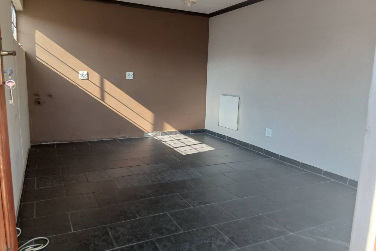An empty living room featuring dark tiled flooring, a ceiling fan, and a wall-mounted heater, offering a blank canvas for interior design.
