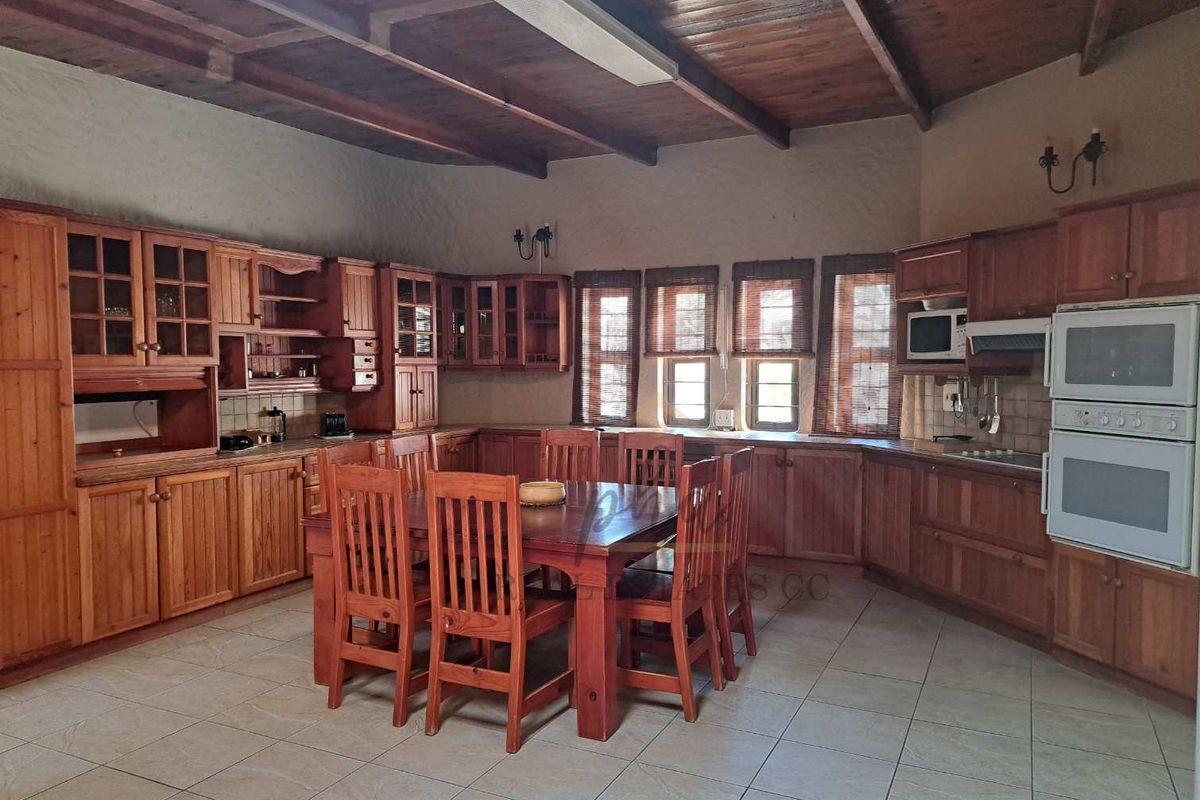 Spacious kitchen featuring extensive timber cabinetry, built-in double oven, and a central dining area under a high exposed timber beam ceiling.