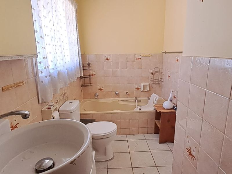 A dated bathroom featuring a built-in bathtub, pedestal basin, and toilet, finished with patterned ceramic wall tiles and floor tiles.