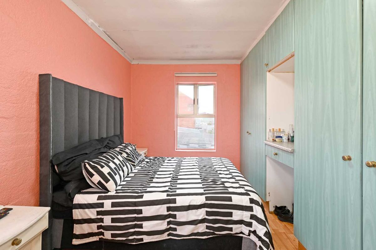 A bedroom featuring built-in cabinetry with a vanity area, pink painted walls, and a window providing natural light.