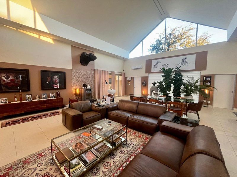 Spacious open-plan living and dining area featuring high vaulted ceilings, large triangular windows, tiled floors, and a built-in fireplace.