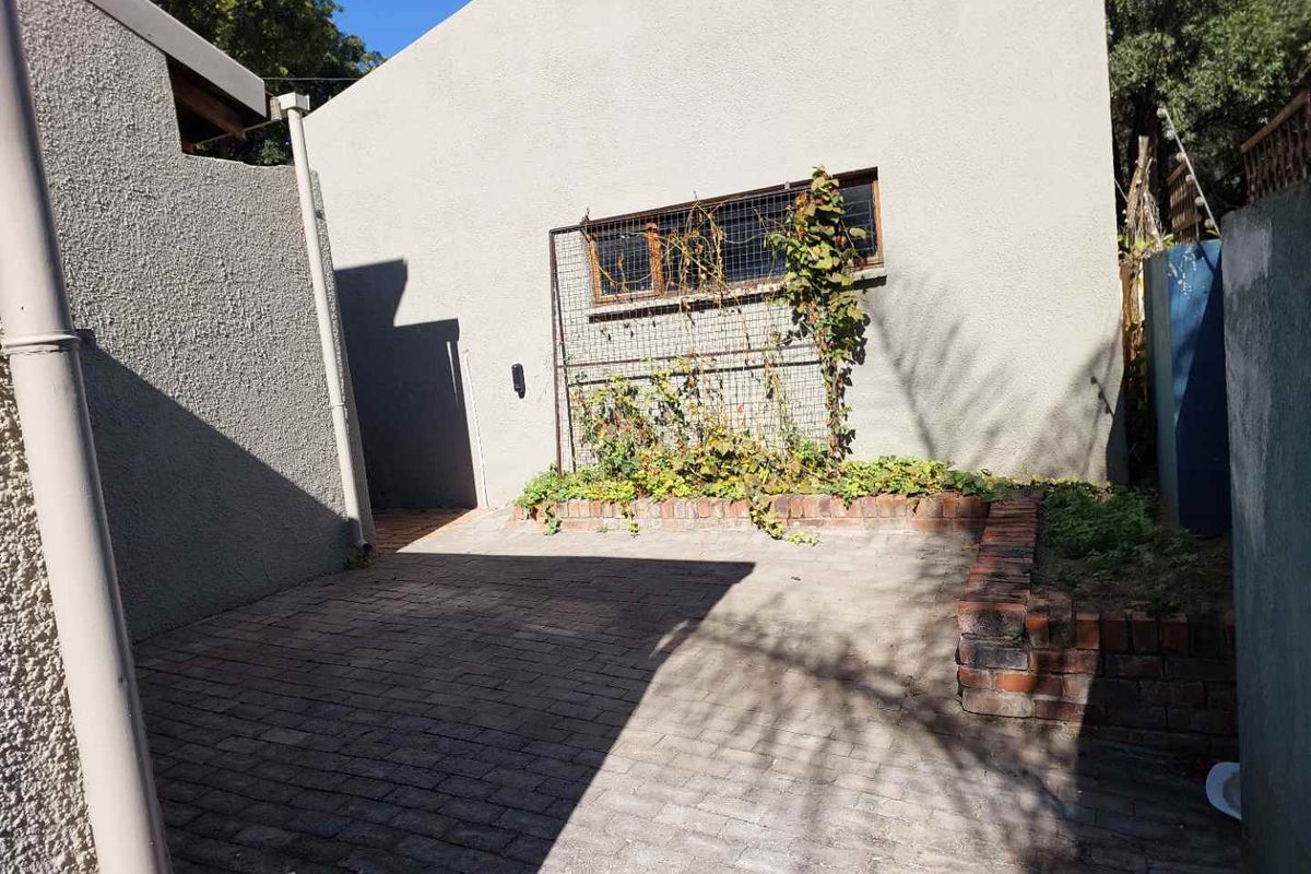 A private rear courtyard area featuring paved flooring, a brick planter box, and a secure window with protective mesh.