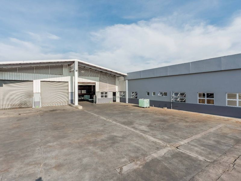 Industrial property exterior featuring a large concrete yard, multiple roller shutter doors, and metal-clad warehouse structures with functional top-hung windows.
