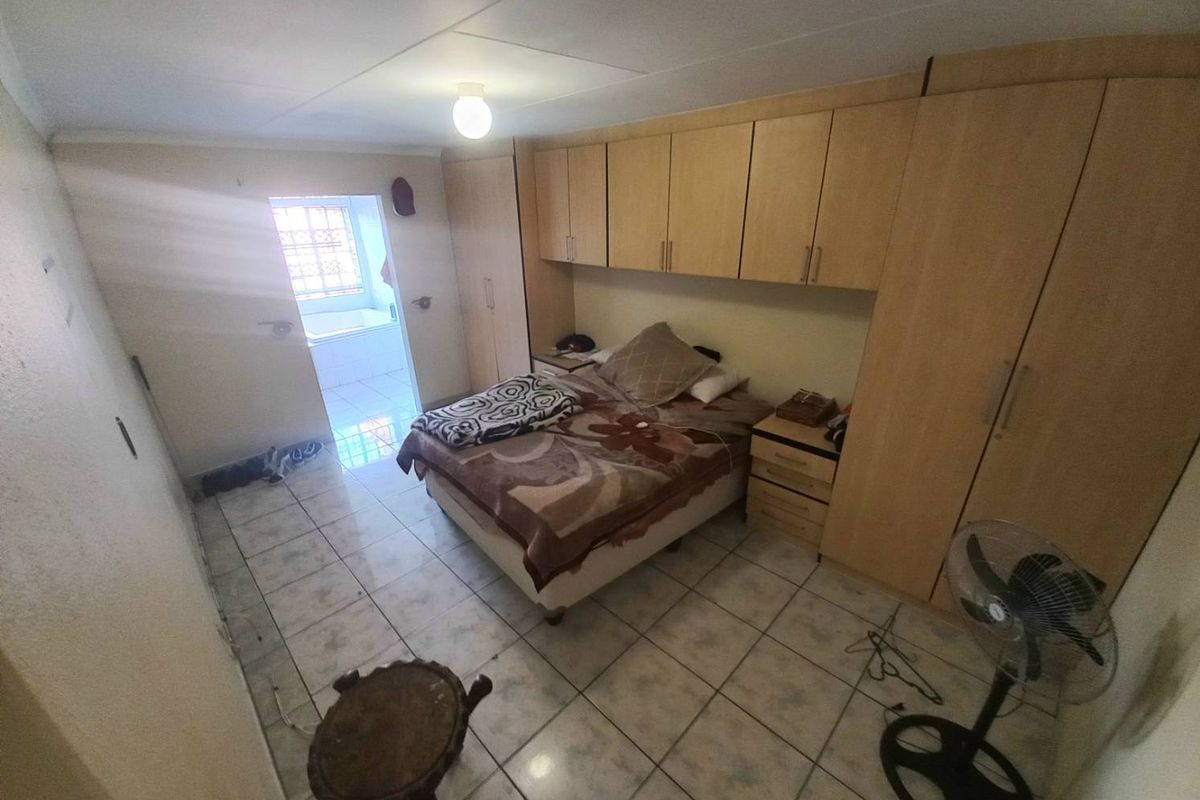 Bedroom featuring built-in wooden cupboards, tiled flooring, and an adjoining en-suite bathroom with a bathtub.