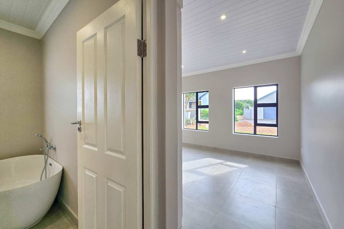 A bright, modern bedroom featuring neutral tones, tiled flooring, recessed lighting, and an en-suite area with a contemporary freestanding bathtub.