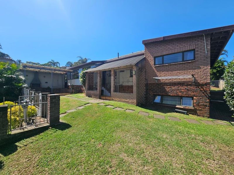 Rear view of a face brick house featuring a covered patio area with a built-in braai and a landscaped garden with a paved walkway.