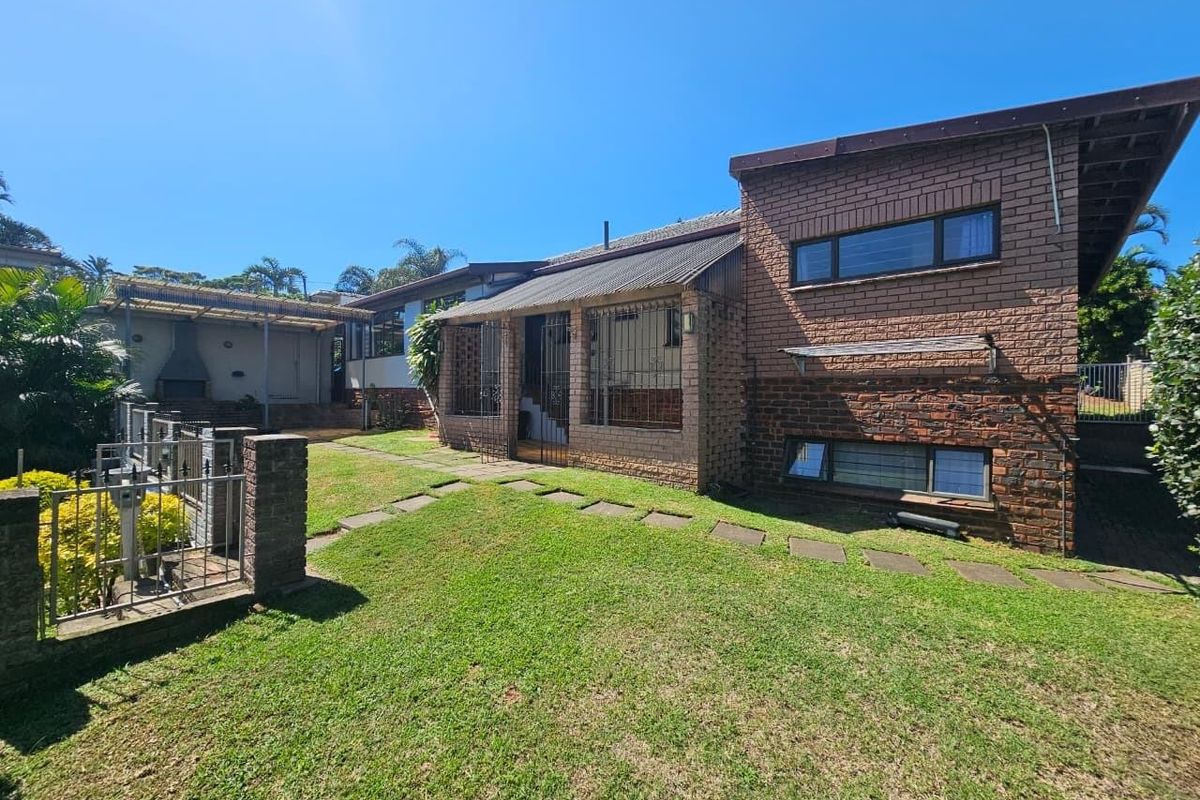 Rear view of a face brick house featuring a covered patio area with a built-in braai and a landscaped garden with a paved walkway.