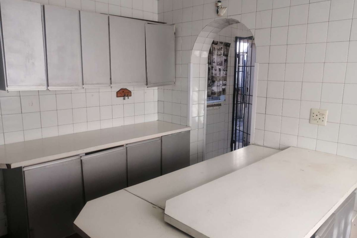 A dated kitchen featuring built-in cabinetry, tiled walls, and a breakfast counter, leading through an arched doorway to an adjacent utility area.