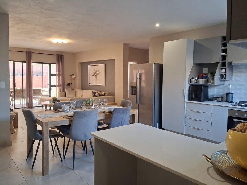 Spacious open-plan living area featuring a modern kitchen with built-in appliances, dining space, and seamless flow to an outdoor patio through sliding glass doors.