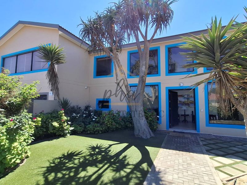 Front exterior view of a double-story guest house featuring a paved walkway, artificial lawn, and distinctive blue-trimmed window frames.