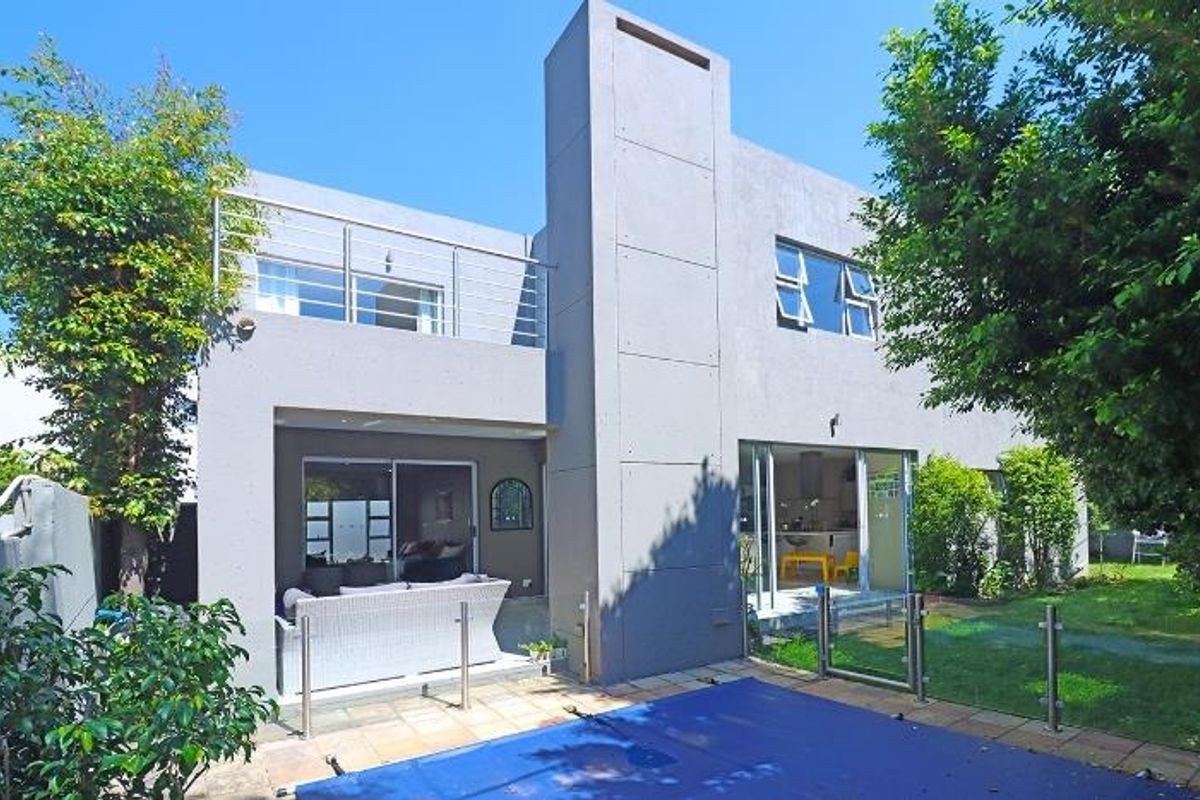 Rear view of a modern double-story cluster home featuring a swimming pool, paved patio area, and an upper-level balcony with stainless steel railings.
