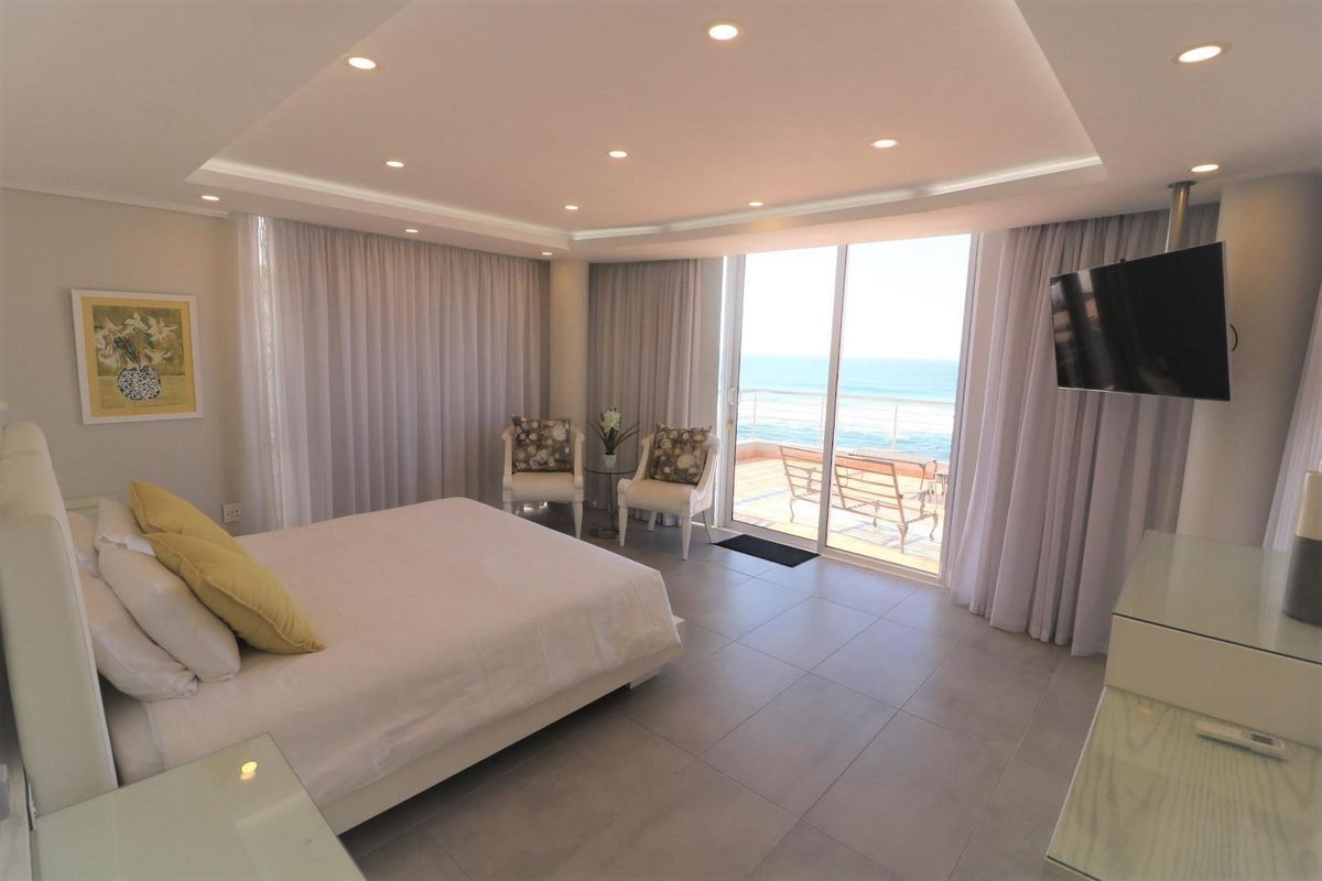Spacious bedroom featuring modern tiled flooring, recessed ceiling lighting, and large sliding glass doors opening onto a private balcony with ocean views.