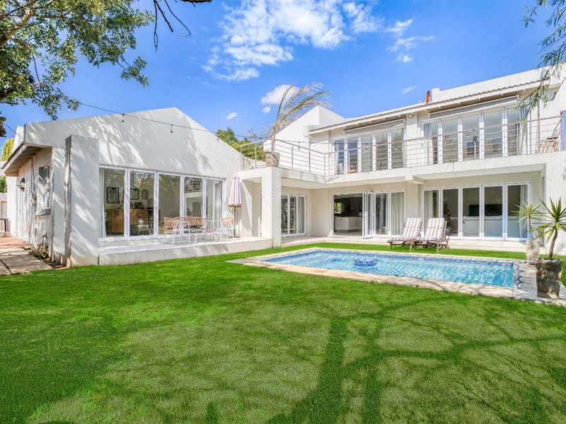 Spacious rear exterior featuring a well-maintained lawn, a swimming pool, a paved patio area, and a two-story building with multiple sliding glass doors.