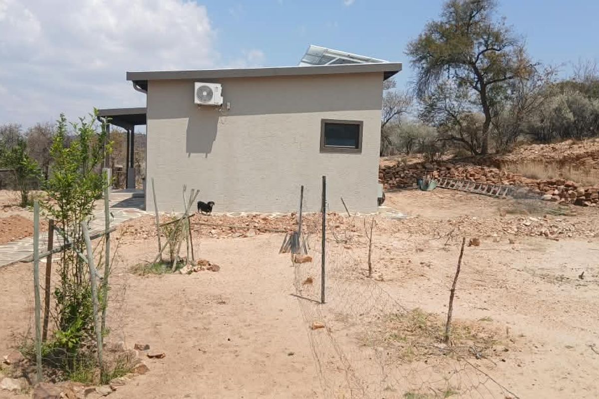 Rear view of the property showing the exterior wall, mounted air conditioning unit, solar panels on the roof, and surrounding natural landscape.