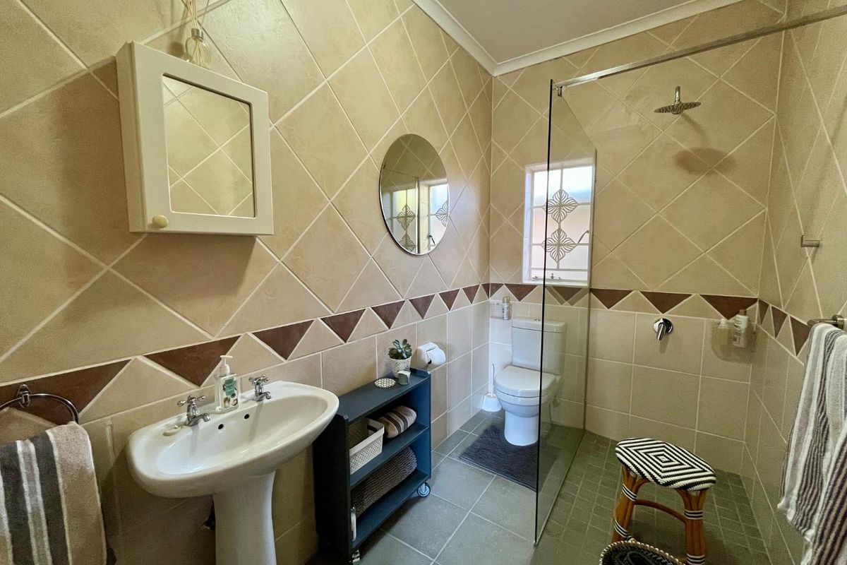 A functional bathroom featuring a pedestal basin, a glass-enclosed walk-in shower, and a toilet, finished with neutral wall tiles and floor tiling.
