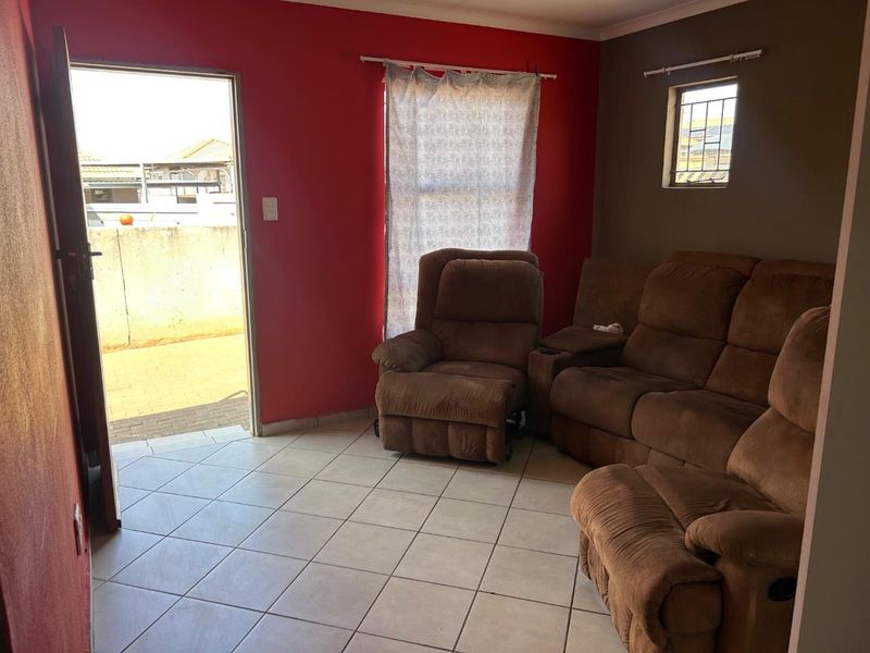 A living room featuring tiled flooring, a small window with security bars, and direct access to an outdoor area.