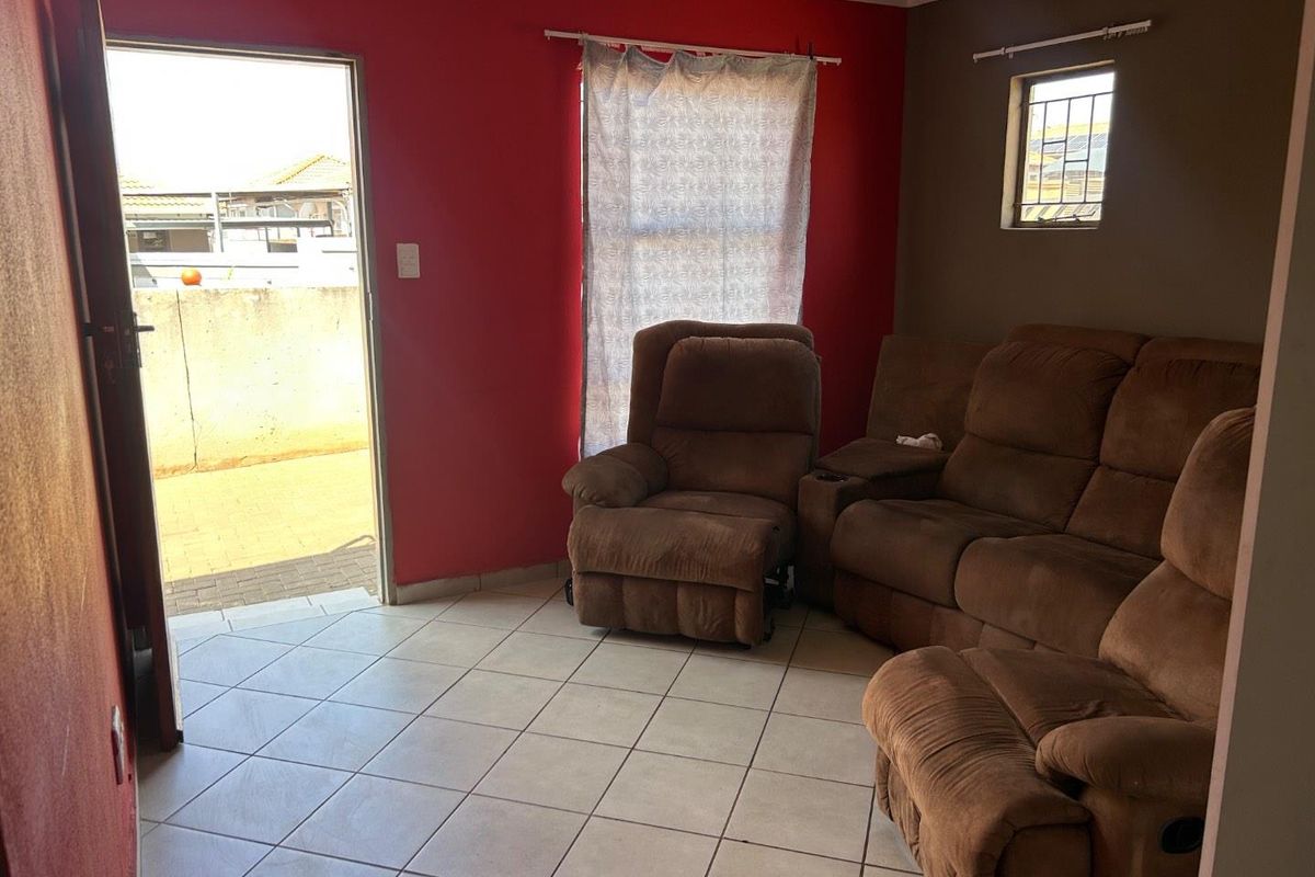 A living room featuring tiled flooring, a small window with security bars, and direct access to an outdoor area.