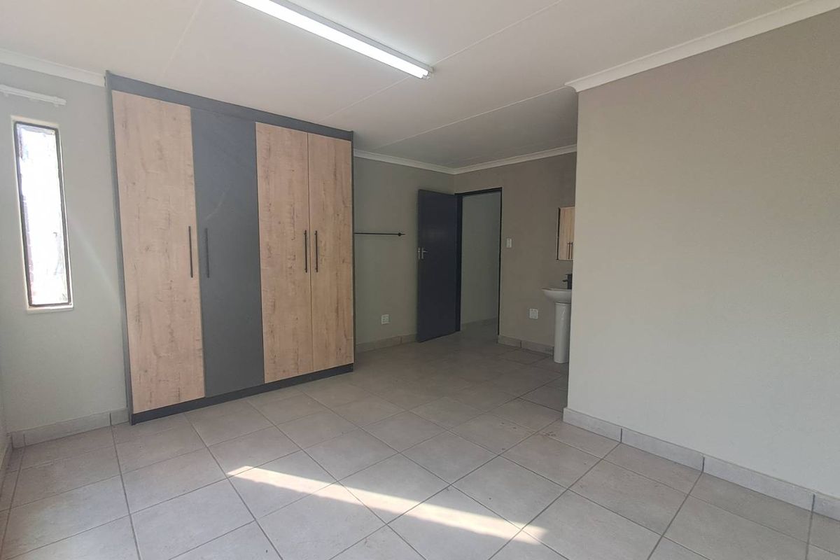A clean, empty bedroom featuring modern built-in cupboards, tiled flooring, and an en-suite pedestal basin area.