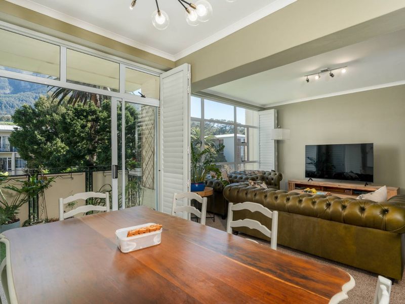 Spacious open-plan living and dining area featuring large sliding glass doors, plantation shutters, and abundant natural light with views of the surrounding greenery.