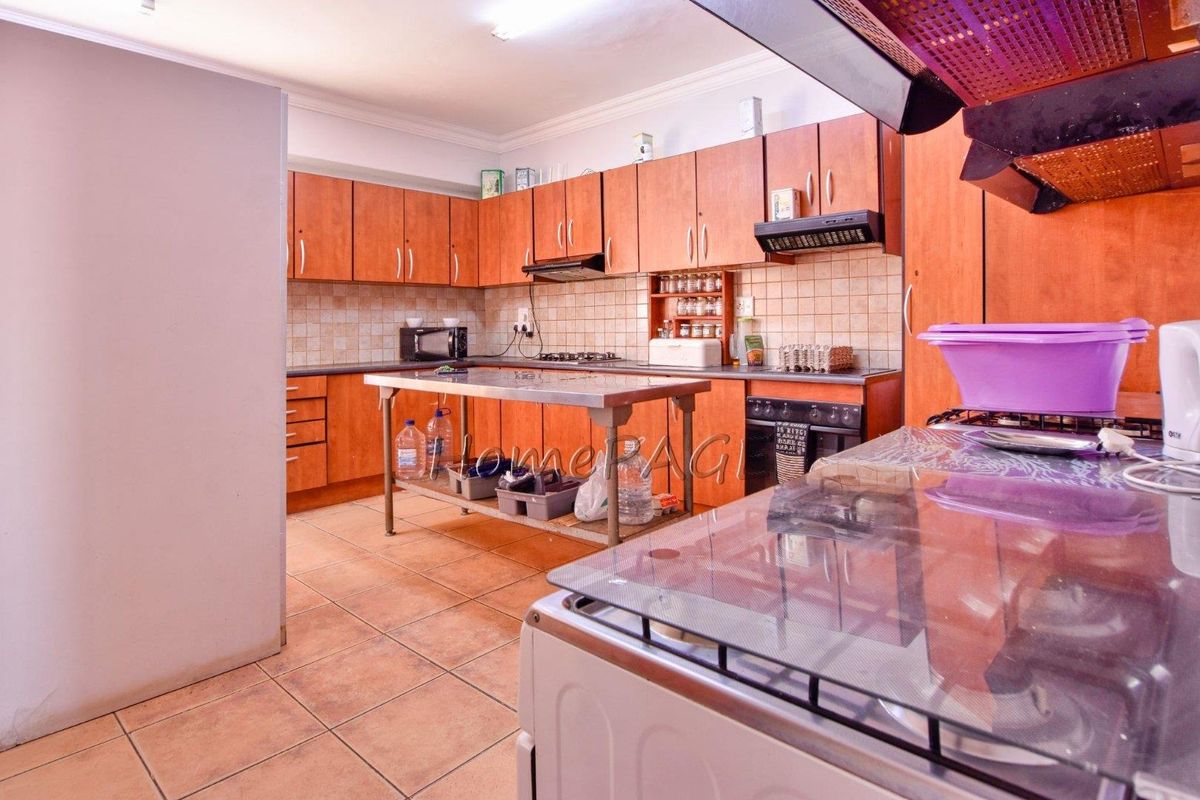 A functional kitchen featuring wooden cabinetry, tiled backsplash, built-in oven, extractor fan, and a central stainless steel prep table.