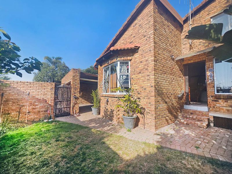 Rear view of a face brick townhouse featuring a paved patio area, bay window, and adjacent carport structure.