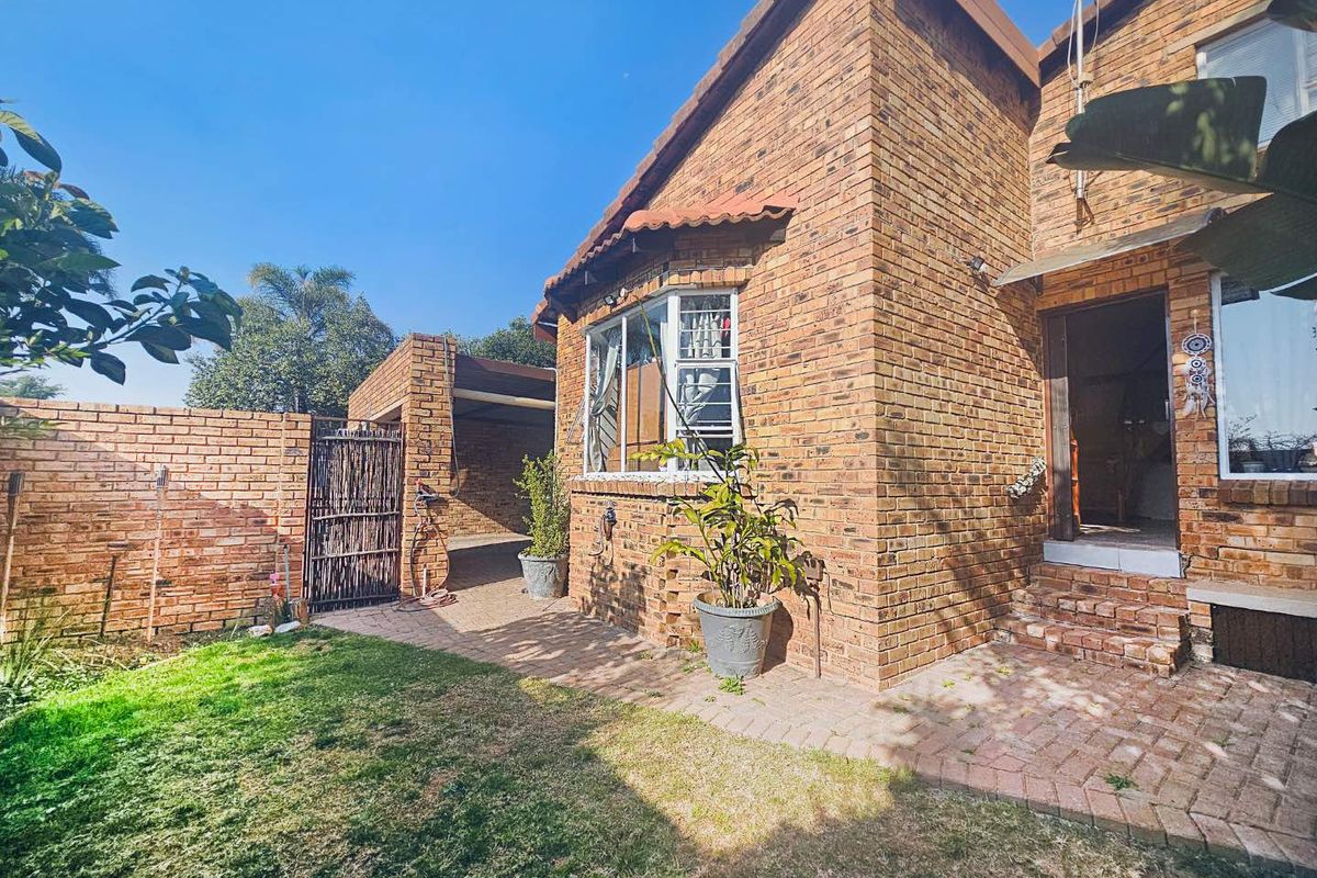 Rear view of a face brick townhouse featuring a paved patio area, bay window, and adjacent carport structure.