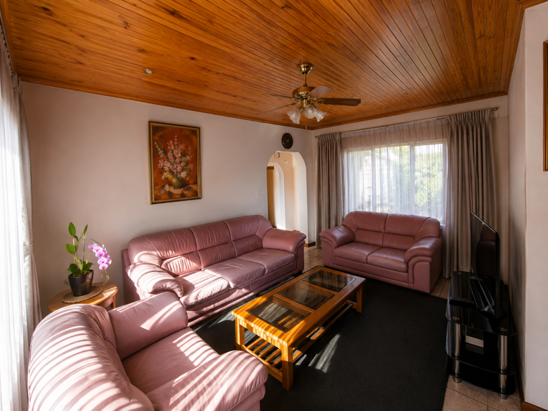 A comfortable living room featuring a warm timber tongue and groove ceiling, a central ceiling fan, and a classic arched doorway.