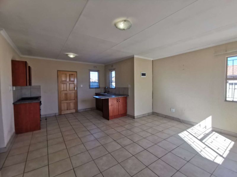 An open-plan living and kitchen area featuring tiled flooring, built-in cabinetry, and security bars on the windows. The space is vacant and ready for staging.