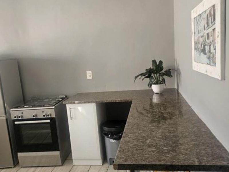 A compact kitchen area featuring a gas stove, oven, granite countertops, and tiled flooring, providing a functional workspace.