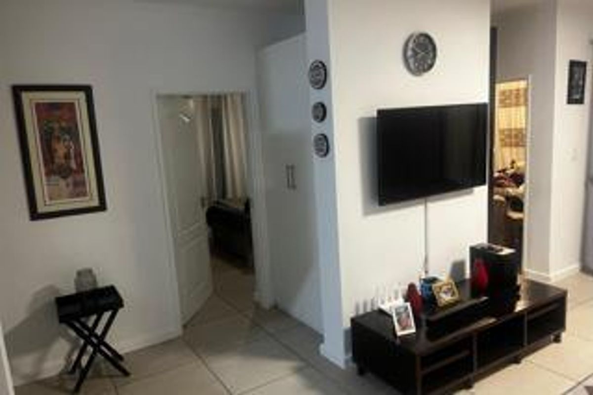 A view of the living area featuring tiled flooring and a wall-mounted television setup, leading into an adjacent bedroom.