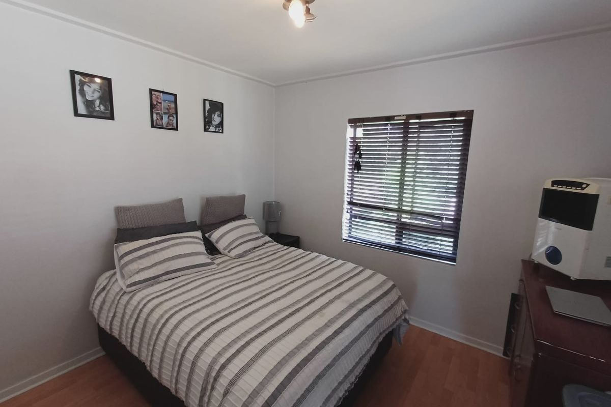 A functional bedroom featuring laminate flooring, a window with venetian blinds, and a central ceiling light fixture.