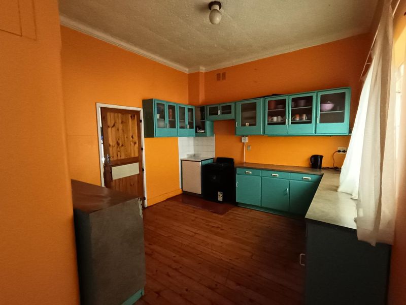 A dated kitchen featuring original timber flooring, teal cabinetry, and a freestanding stove, offering significant potential for a modern renovation.