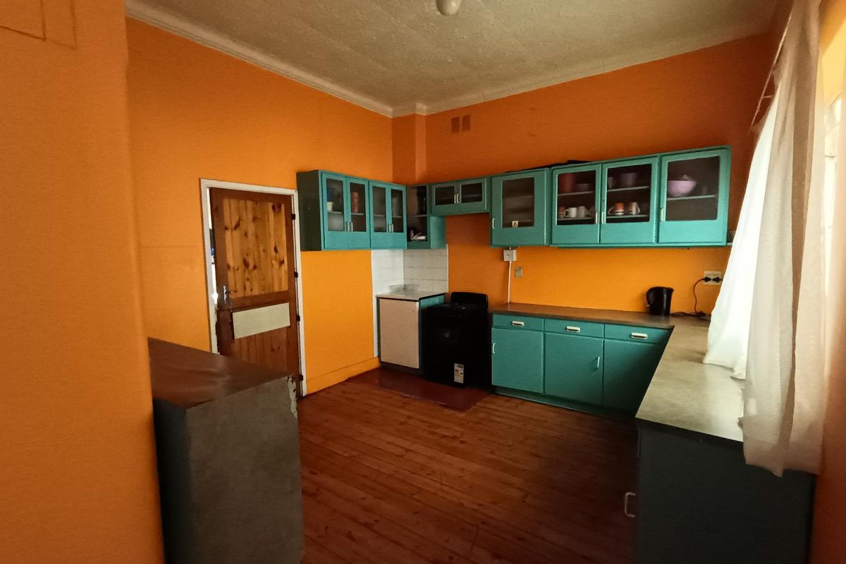 A dated kitchen featuring original timber flooring, teal cabinetry, and a freestanding stove, offering significant potential for a modern renovation.