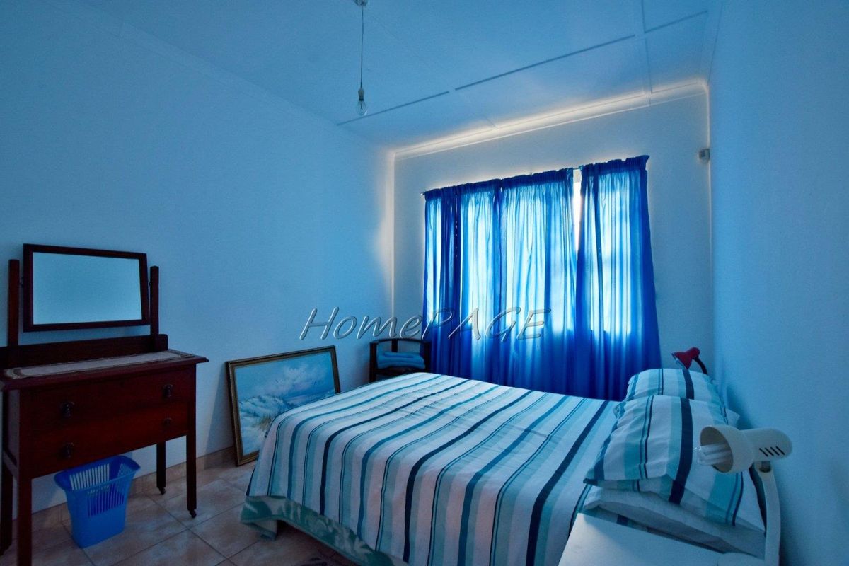 A simple bedroom featuring tiled flooring and large windows with blue curtains, providing a functional and well-lit sleeping space.